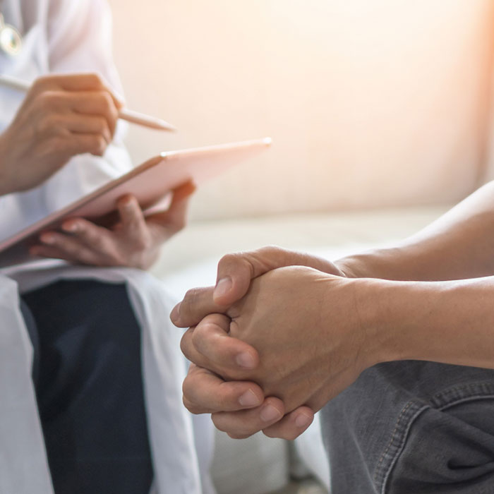 A doctor with a clipboard explaining something with a patient with folded hands