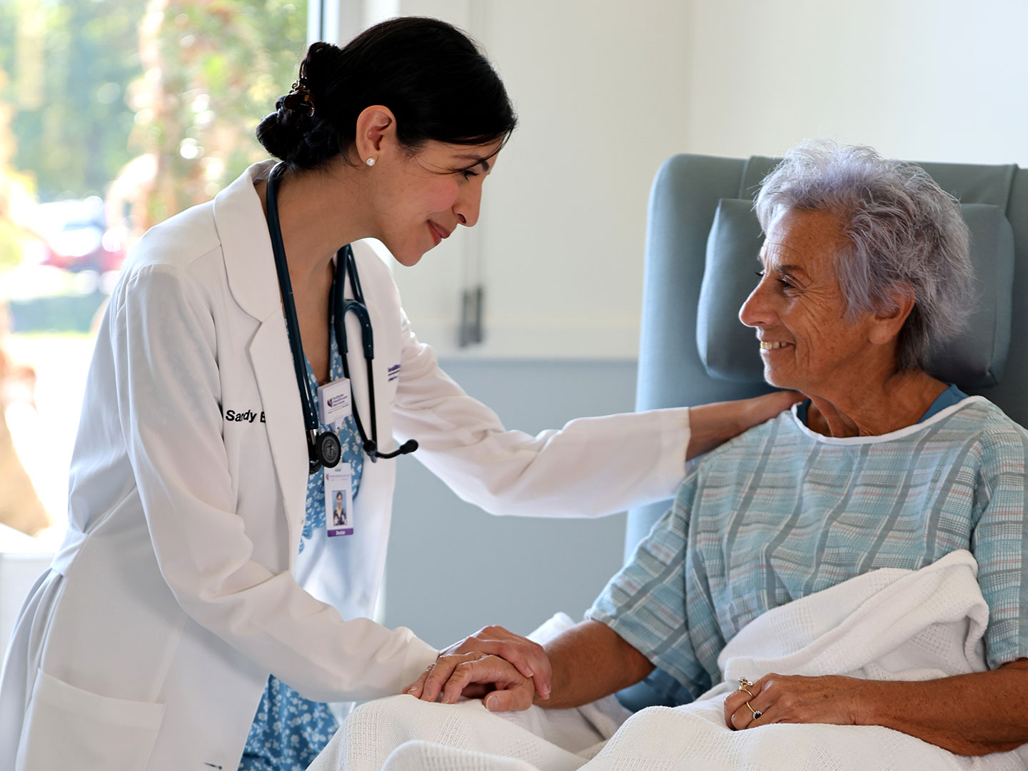 A smiling nurse looks over a patient in a senior living healthcare and hospice facility