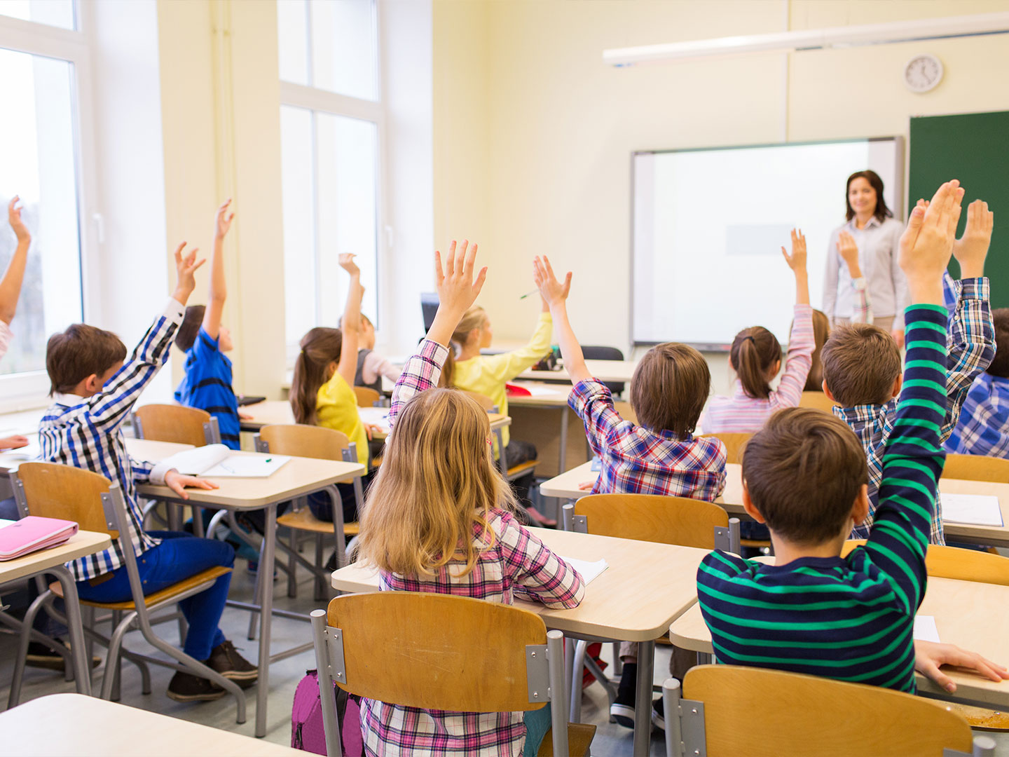 Students excitedly raising their hands in a sunny classroom setting